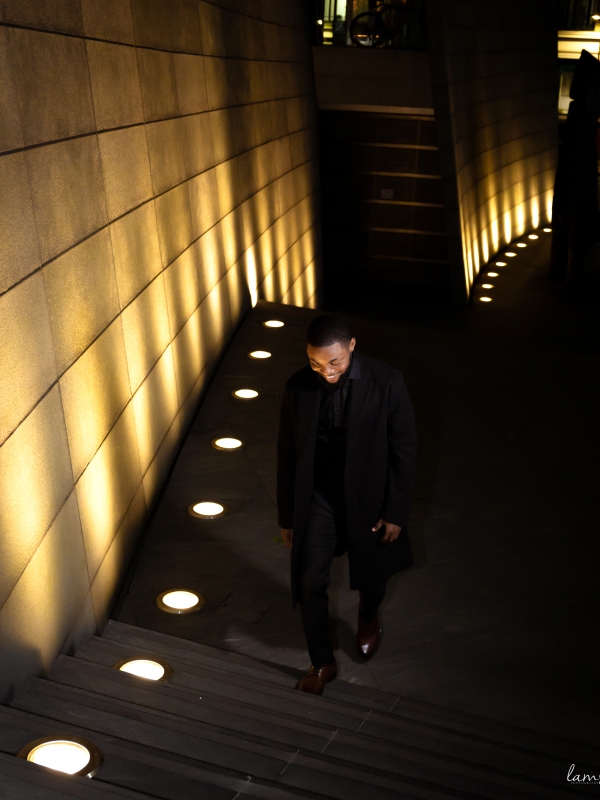 A Man In A Black Suit Walking Down A Modern Staircase Illuminated By Recessed Floor Lights.